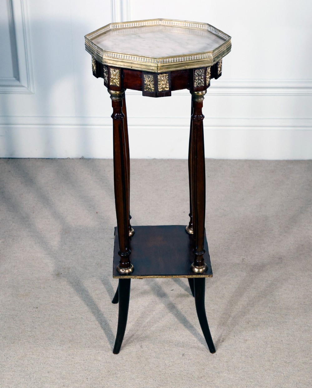A tall French mahogany octagonal occasional table featuring an inset marble top with a pierced brass gallery rail, ormolu mounts, a lower shelf, and slender legs.