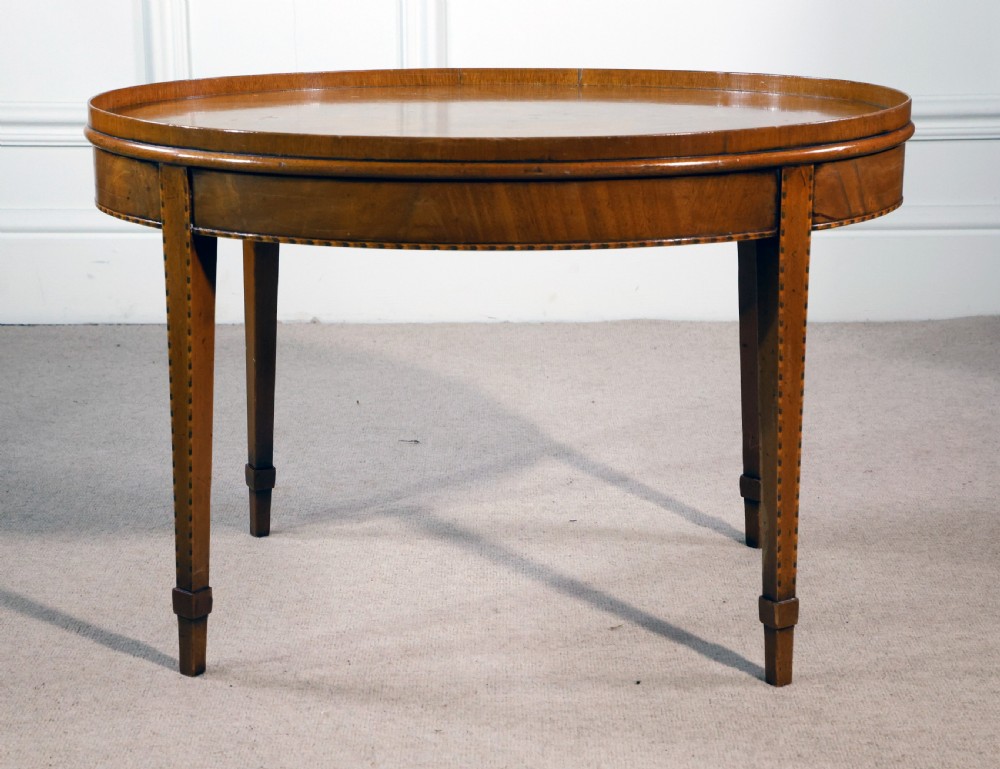 An oval mahogany low table featuring a raised gallery tray top, line inlay along the apron, and four square tapered legs.