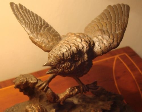 fig 1. A 19th-century bronze sculpture depicting a sparrow with raised wings perched on a branch atop a textured, oval-shaped base.