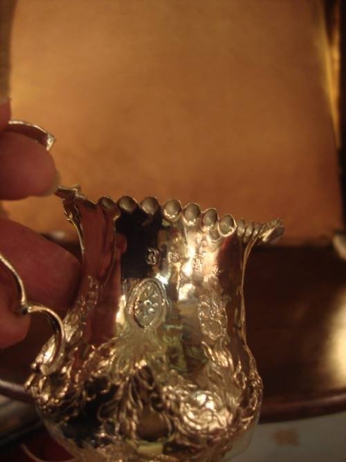 fig 2. A Georgian sterling silver pedestal cream jug featuring chased floral decoration, a scalloped rim, and a double-scroll handle.