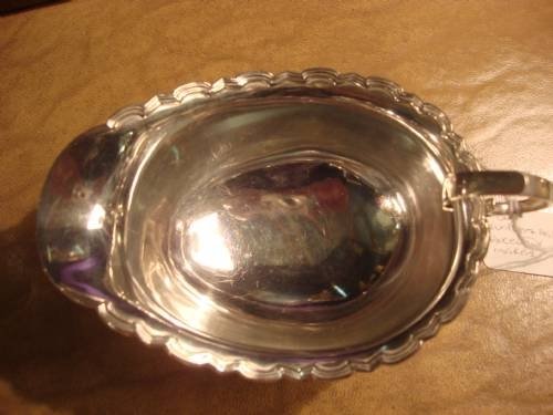 fig 1. A polished solid silver sauce boat featuring a scalloped upper rim, a C-scroll handle, and an oval pedestal base.
