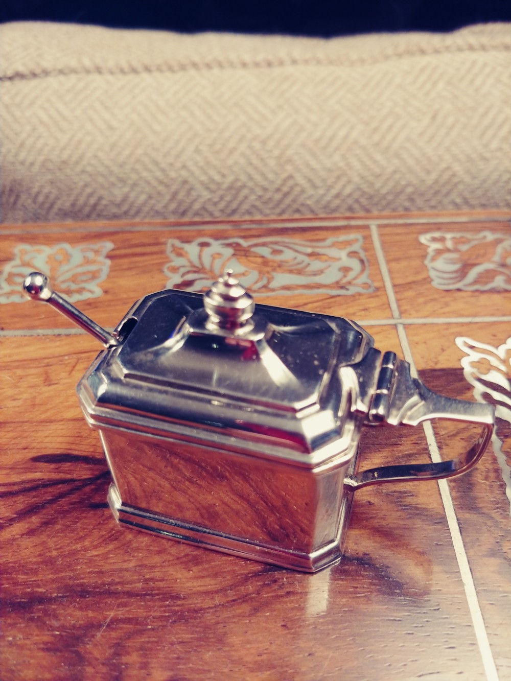 A rectangular solid silver mustard pot with a stepped pagoda lid, tiered finial, and angular handle. View VI