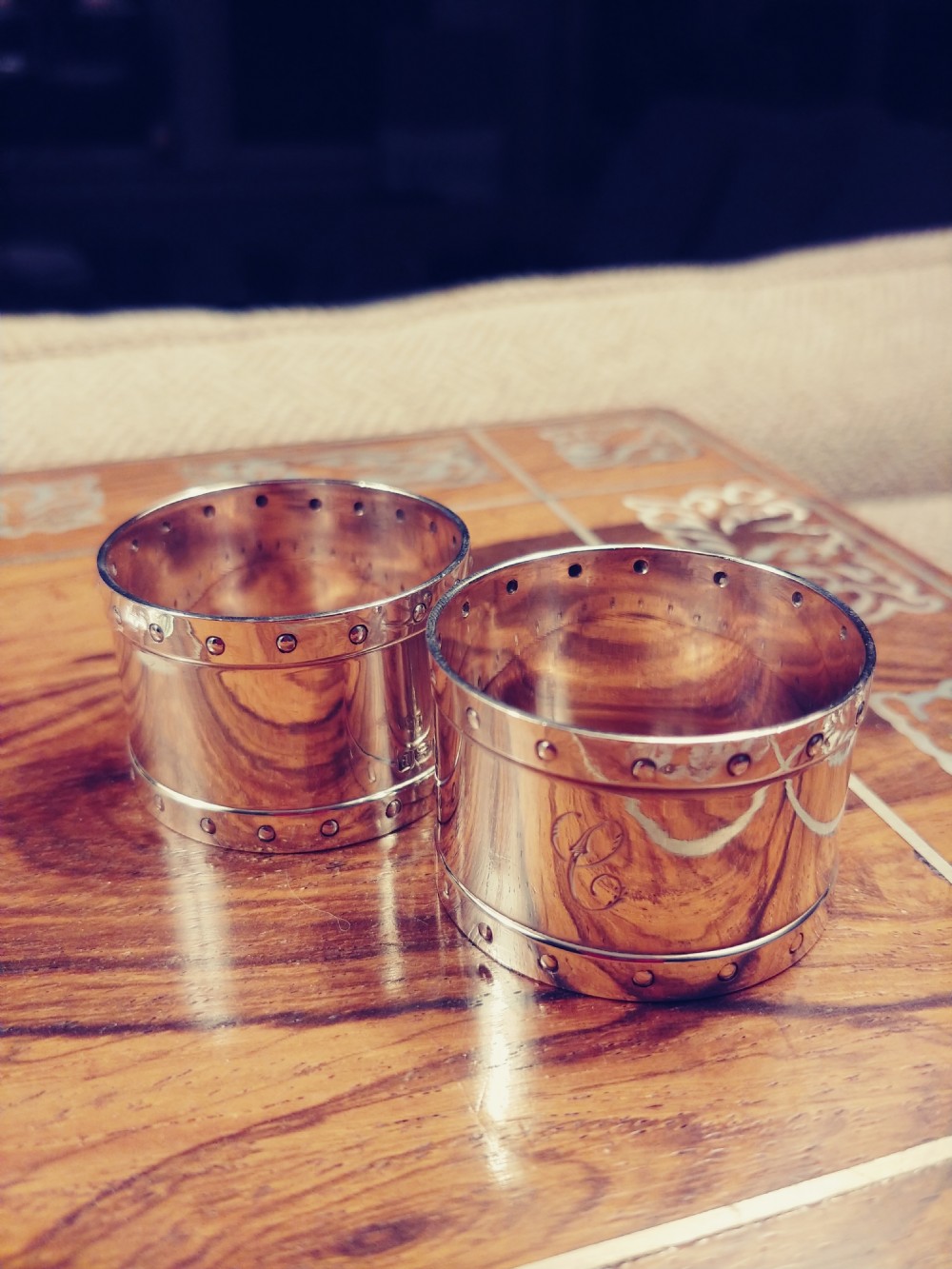 A pair of circular sterling silver napkin rings featuring a studded border design and subtle engraved monograms.