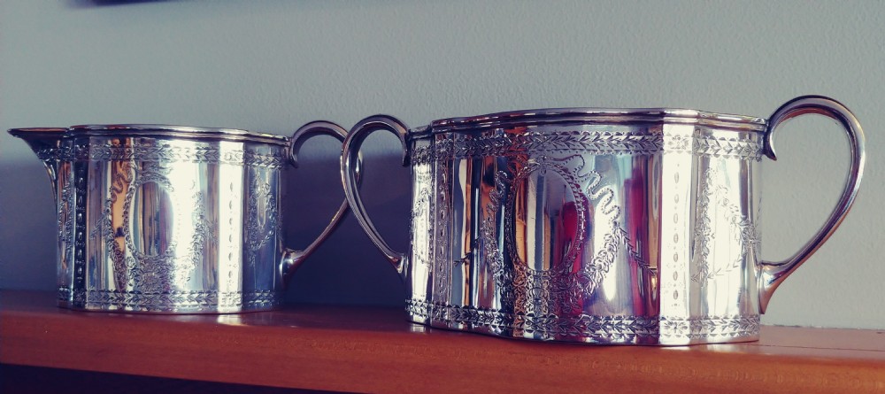A Victorian sterling silver cream jug and matching double-handled sugar bowl featuring engraved garland motifs and curved handles.