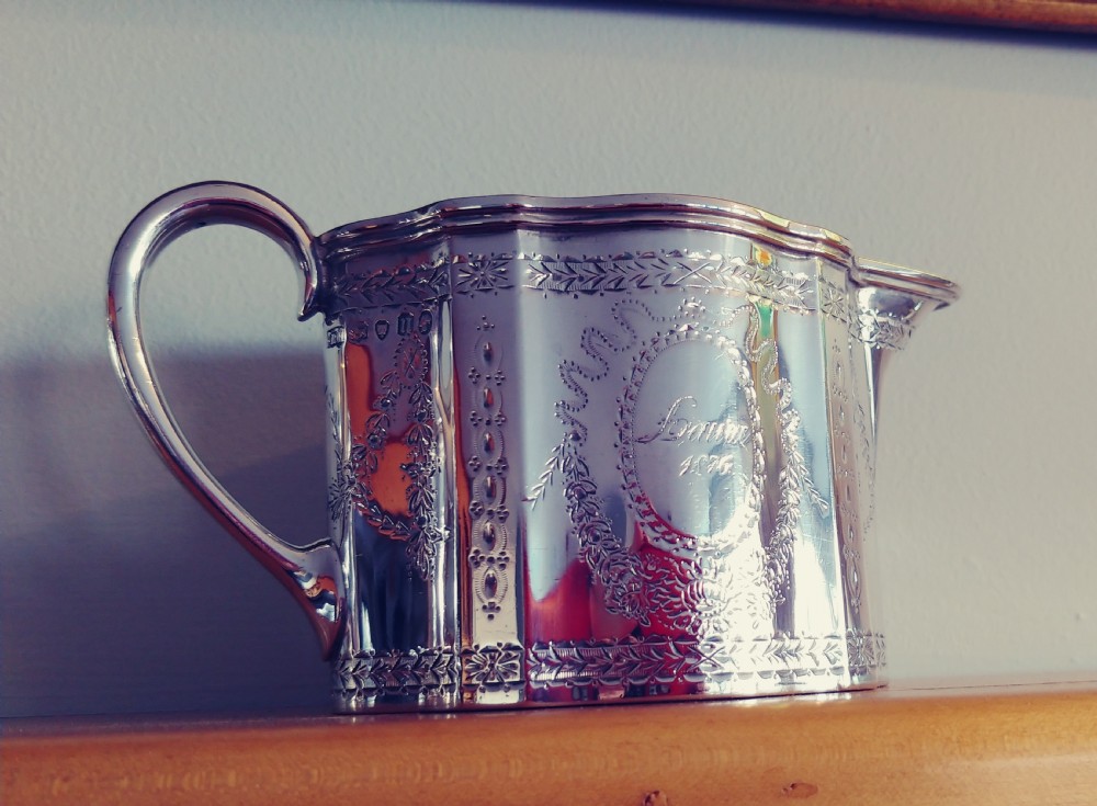A Victorian sterling silver cream jug and matching double-handled sugar bowl featuring engraved garland motifs and curved handles. View V