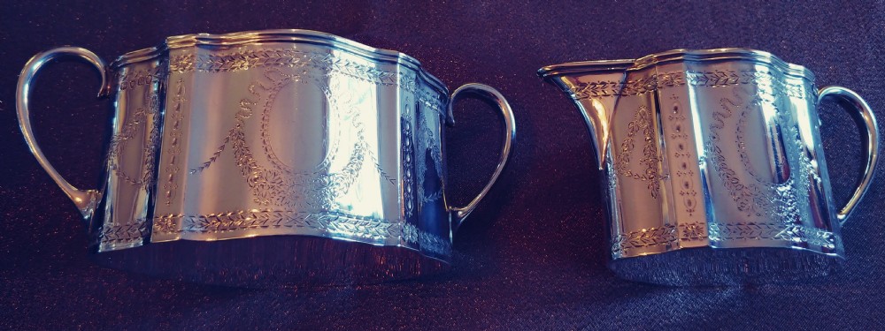 A Victorian sterling silver cream jug and matching double-handled sugar bowl featuring engraved garland motifs and curved handles. View VI