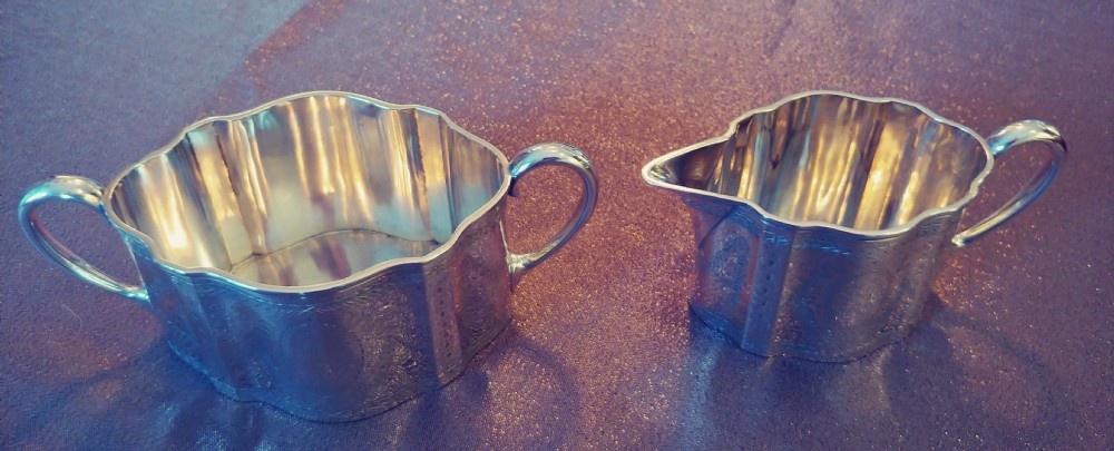 A Victorian sterling silver cream jug and matching double-handled sugar bowl featuring engraved garland motifs and curved handles. View VII