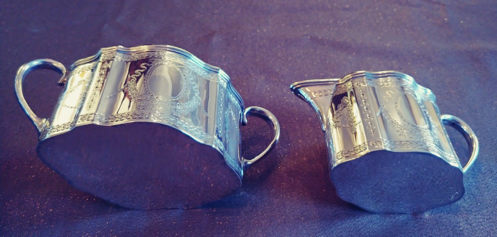 A Victorian sterling silver cream jug and matching double-handled sugar bowl featuring engraved garland motifs and curved handles. View VIII