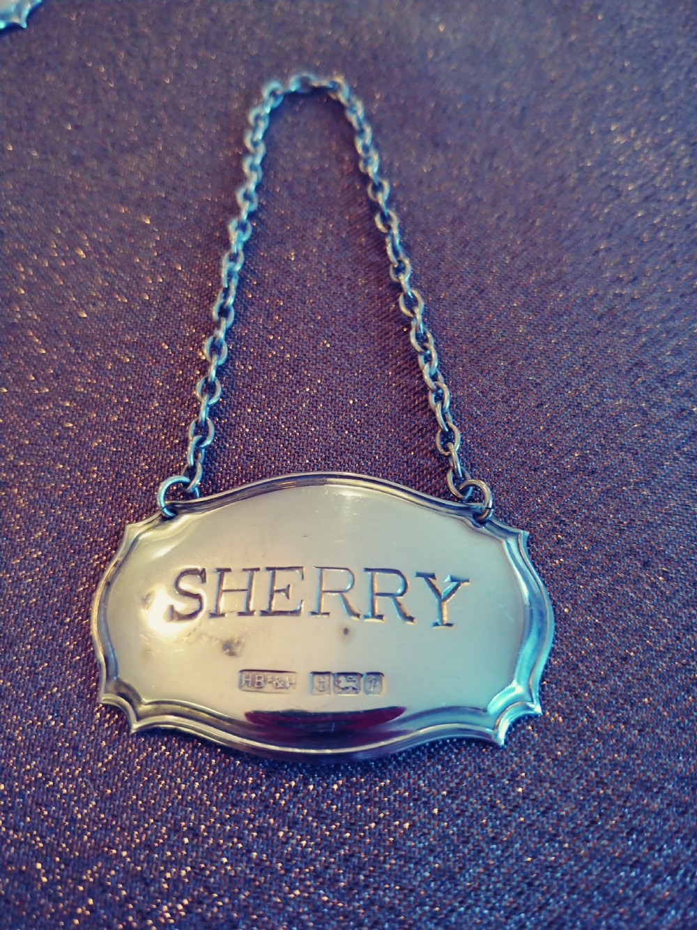 A set of three shaped sterling silver decanter labels engraved with Sherry, Whisky, and Brandy, suspended from fine link chains. View IV