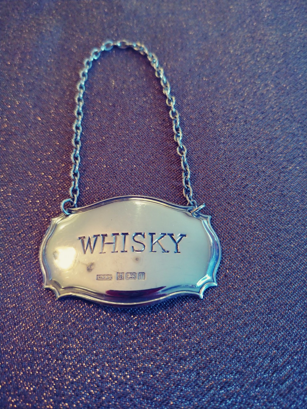 A set of three shaped sterling silver decanter labels engraved with Sherry, Whisky, and Brandy, suspended from fine link chains. View III