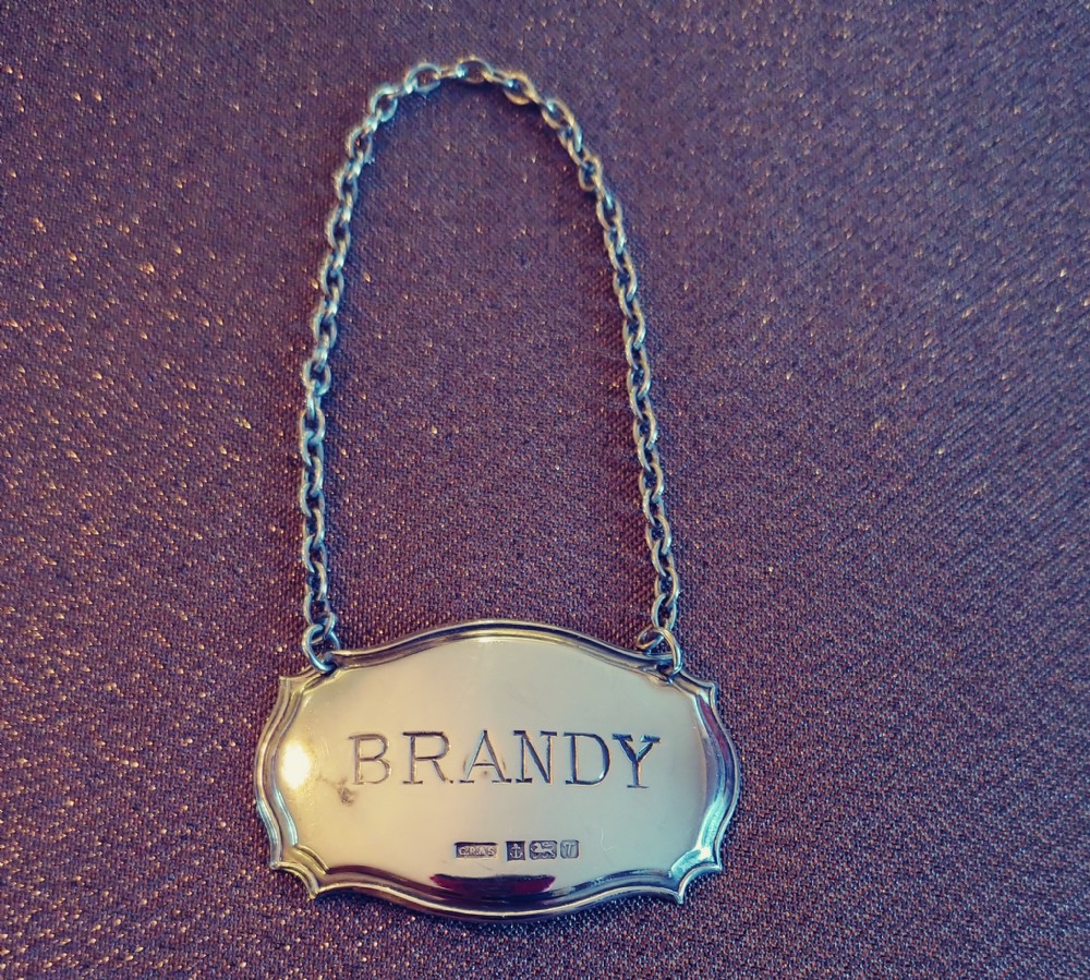 A set of three shaped sterling silver decanter labels engraved with Sherry, Whisky, and Brandy, suspended from fine link chains. View II