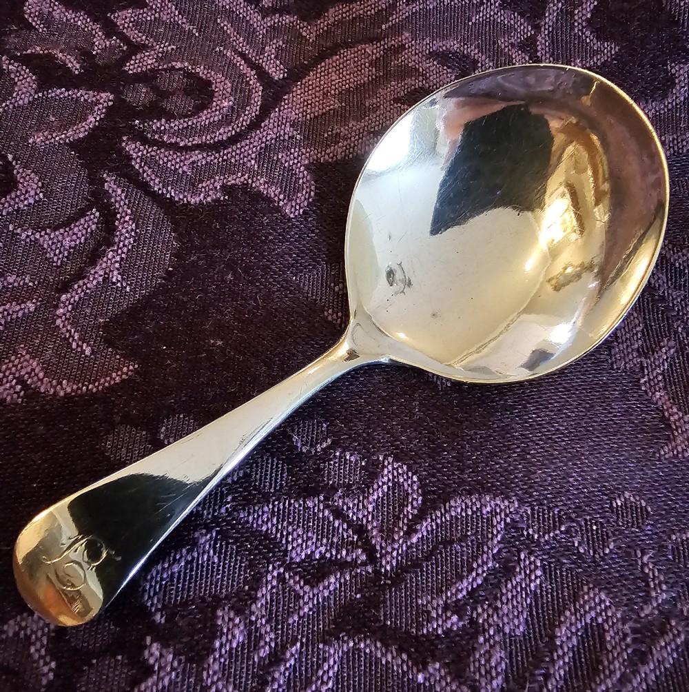 A Georgian sterling silver tea caddy spoon featuring a smooth oval bowl and a tapered handle with an engraved monogram.