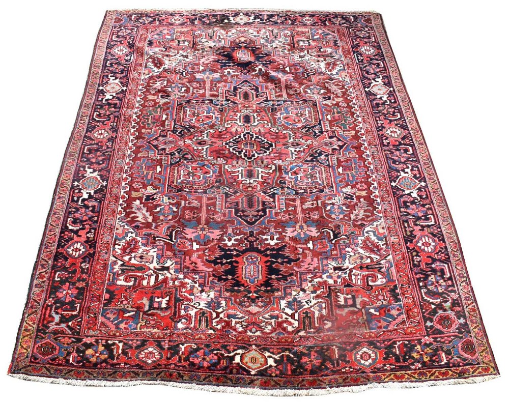 A hand-knotted Heriz wool carpet featuring a central geometric medallion framed by red, navy blue, and light blue floral borders.