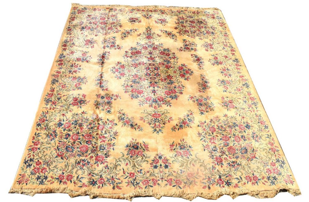 A large rectangular hand-knotted Persian Kirman wool carpet featuring a central floral medallion on a cream ground.