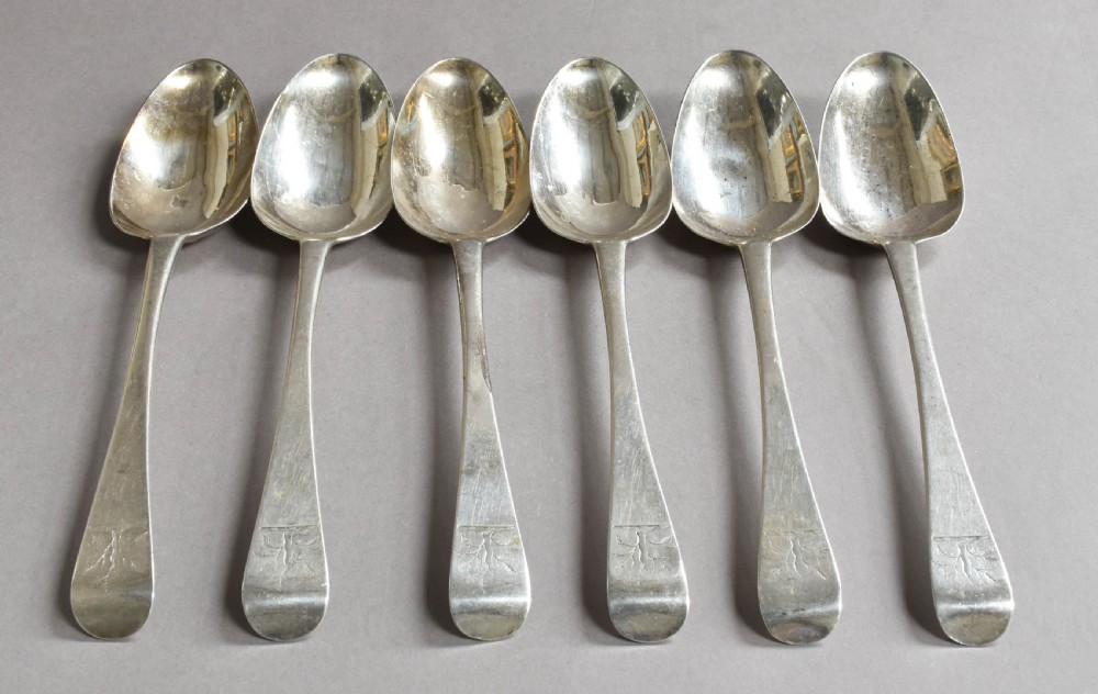 A set of six George III Irish sterling silver table spoons with engraved crests on the handle terminals arranged side by side.