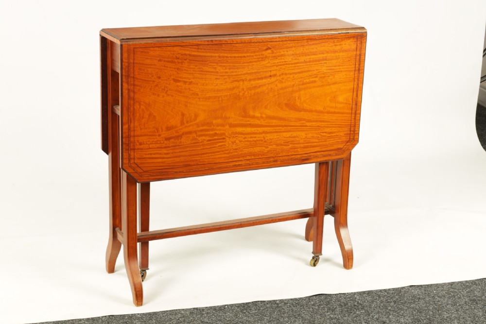A nineteenth-century figured satinwood Sutherland table featuring two drop flaps, slatted upright legs, splayed feet, and small brass castors. View II