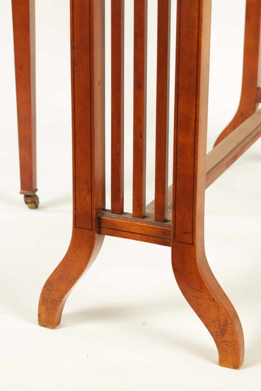 A nineteenth-century figured satinwood Sutherland table featuring two drop flaps, slatted upright legs, splayed feet, and small brass castors. View III