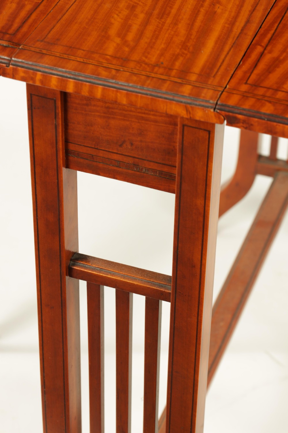 A nineteenth-century figured satinwood Sutherland table featuring two drop flaps, slatted upright legs, splayed feet, and small brass castors. View IV