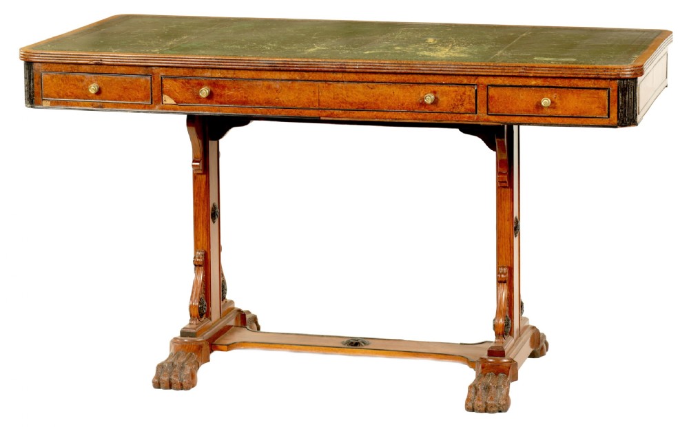 An antique amboyna and rosewood library table featuring a green leather inset top, frieze drawers with brass knobs, trestle legs, and carved lion paw feet.