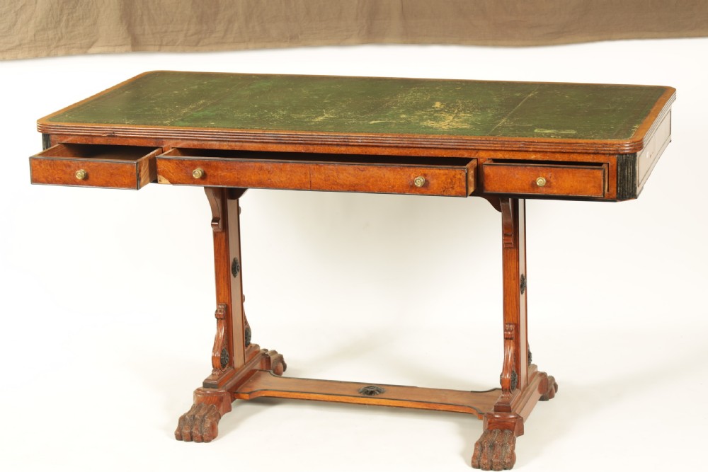 An antique amboyna and rosewood library table featuring a green leather inset top, frieze drawers with brass knobs, trestle legs, and carved lion paw feet. View II