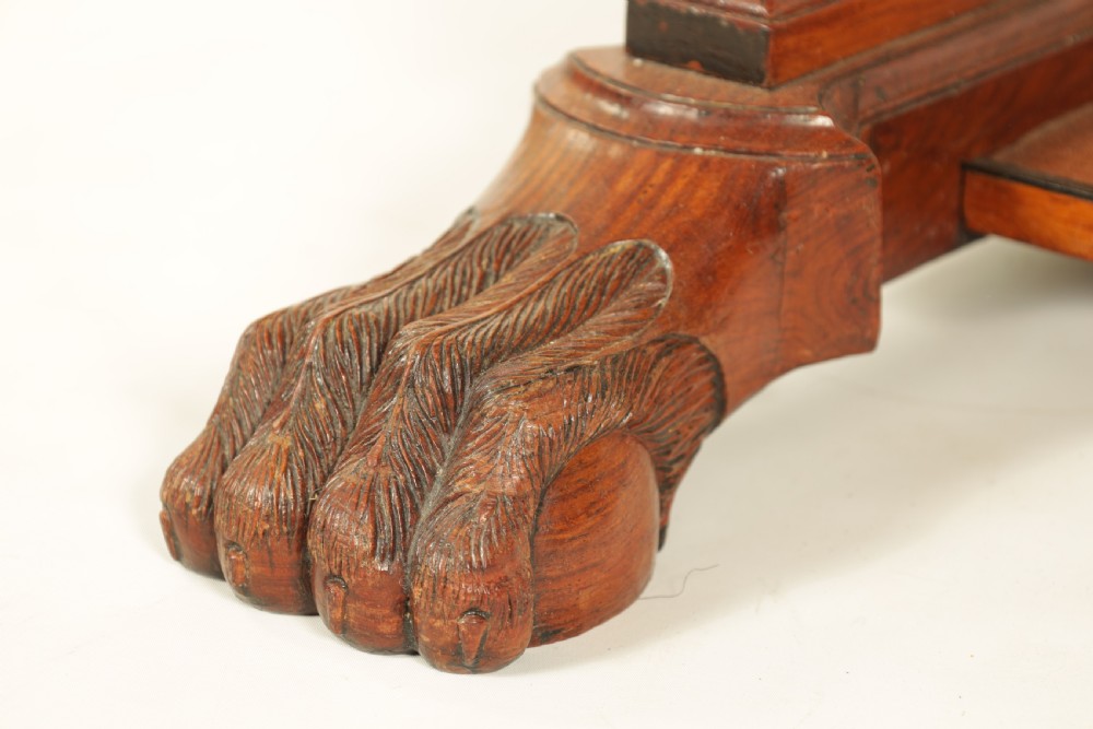 An antique amboyna and rosewood library table featuring a green leather inset top, frieze drawers with brass knobs, trestle legs, and carved lion paw feet. View III