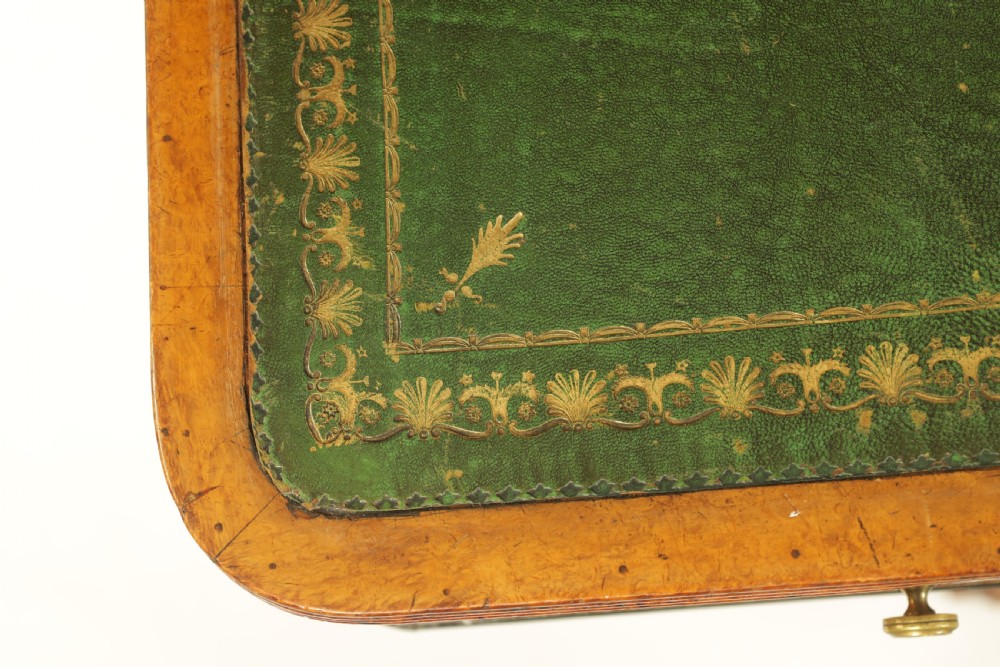 An antique amboyna and rosewood library table featuring a green leather inset top, frieze drawers with brass knobs, trestle legs, and carved lion paw feet. View VII