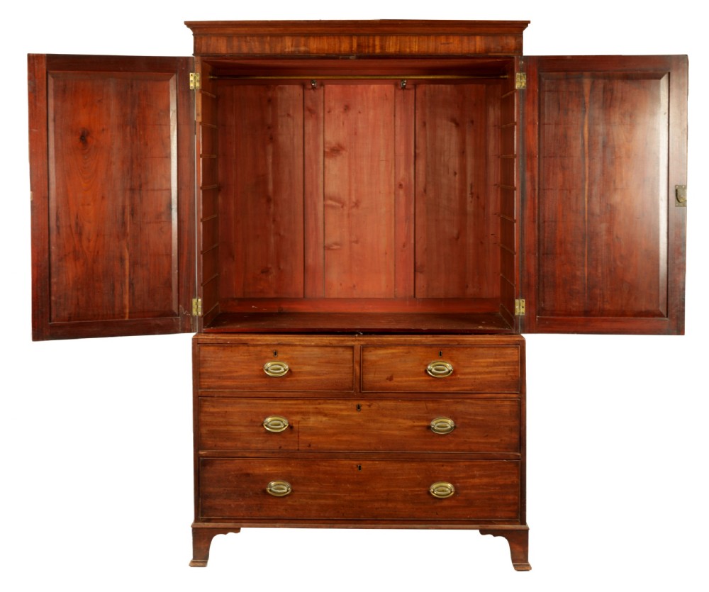 A George III mahogany hanging clothes press featuring two flame mahogany panelled doors over four drawers with brass handles, raised on bracket feet. View II