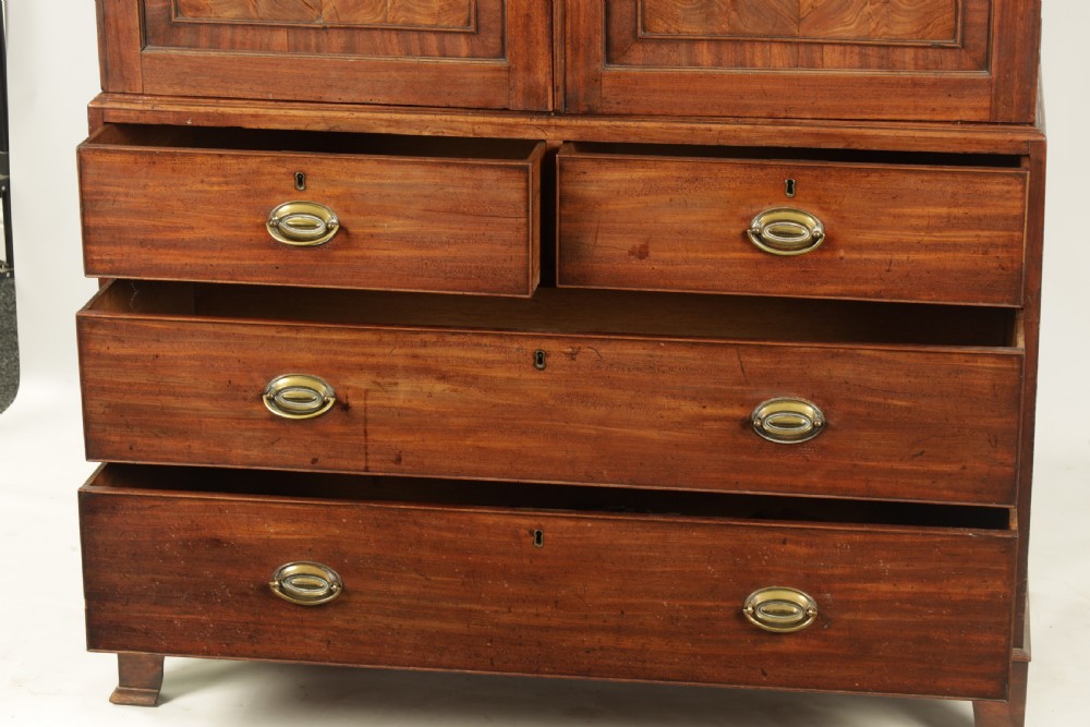A George III mahogany hanging clothes press featuring two flame mahogany panelled doors over four drawers with brass handles, raised on bracket feet. View IV