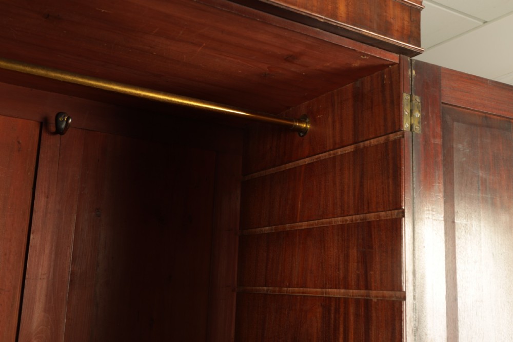 A George III mahogany hanging clothes press featuring two flame mahogany panelled doors over four drawers with brass handles, raised on bracket feet. View VII