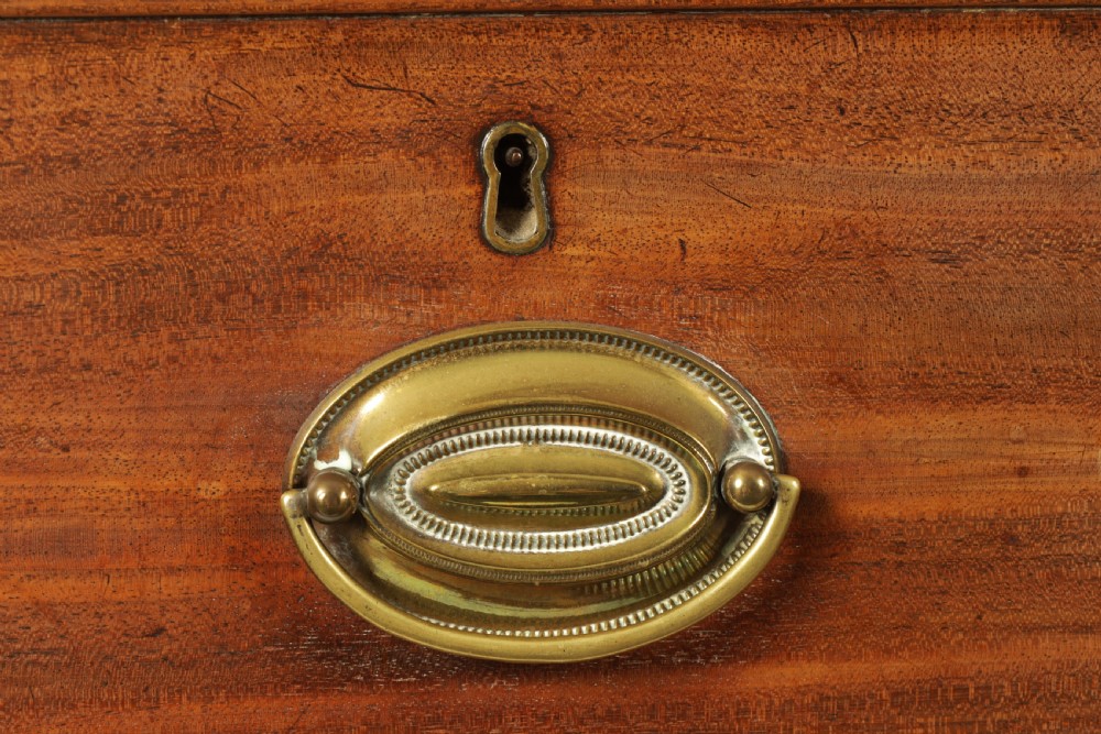 A George III mahogany hanging clothes press featuring two flame mahogany panelled doors over four drawers with brass handles, raised on bracket feet. View VIII