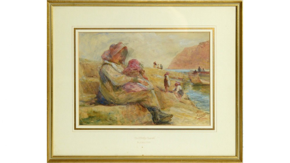 A framed watercolour painting depicting figures on a sandy coastal shoreline with cliffs in the background.