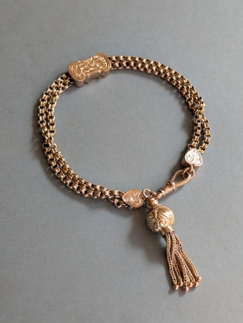 fig 1. An antique 9ct gold double chain bracelet featuring engraved heart-shaped end pieces, a swivel clasp, and a hanging gold tassel charm.