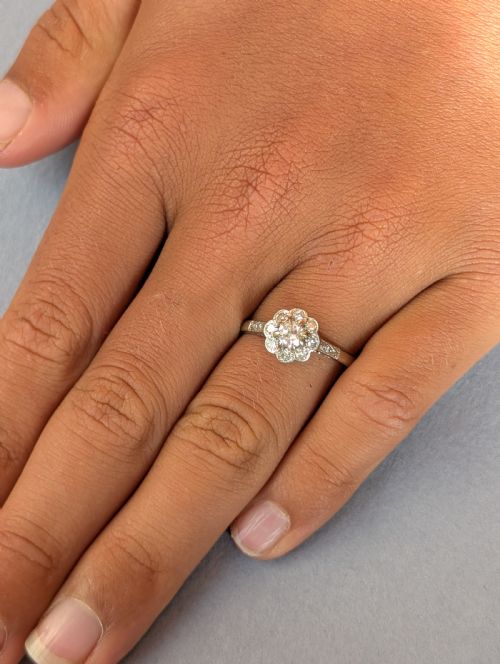 fig 1. An Art Deco diamond daisy cluster ring with a circular central diamond surrounded by eight smaller diamonds set on a polished band with detailed shoulders.