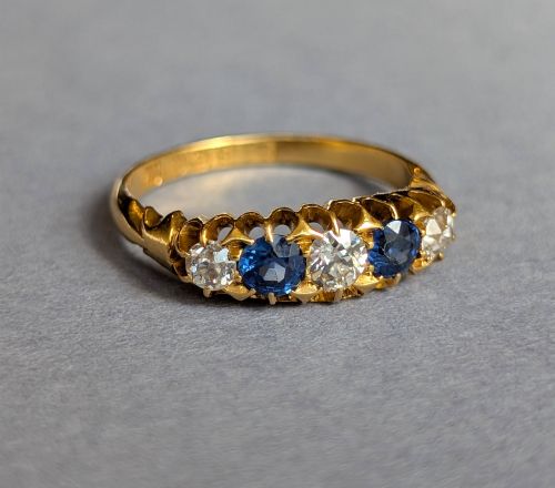 fig 2. An Edwardian 18ct yellow gold five-stone ring featuring alternating blue sapphires and old cut diamonds set within a carved scroll head.