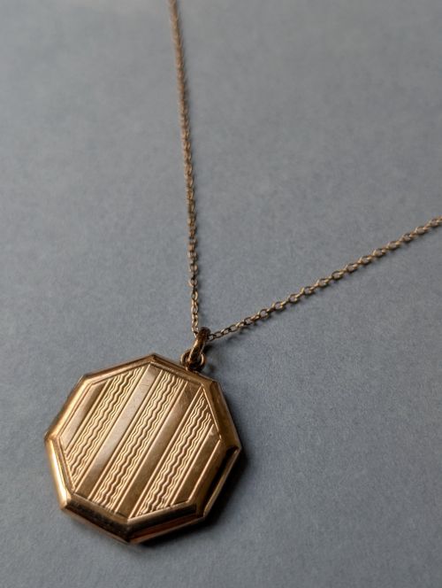fig 2. An octagonal 9ct rose gold locket featuring engine-turned geometric engraving suspended from a fine gold chain.