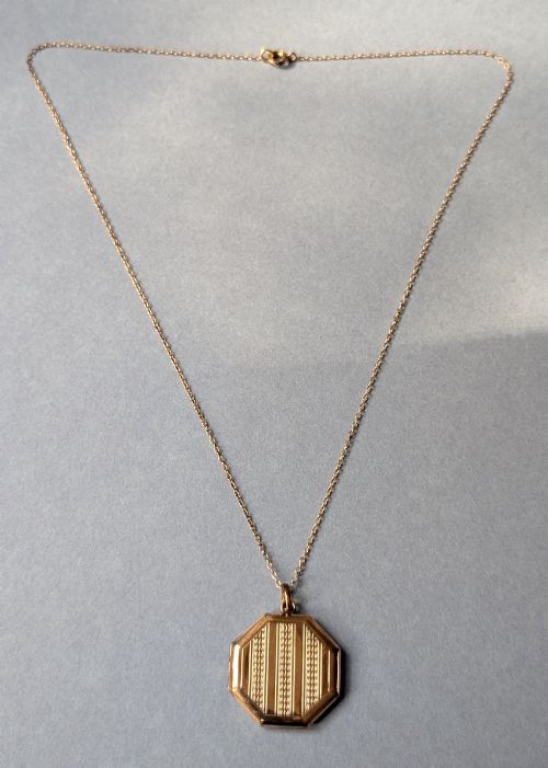 fig 3. An octagonal 9ct rose gold locket featuring engine-turned geometric engraving suspended from a fine gold chain.