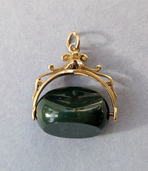fig 1. An antique 9ct gold spinning fob pendant featuring a polished dark green bloodstone within an ornate scrolled gold swivel frame.