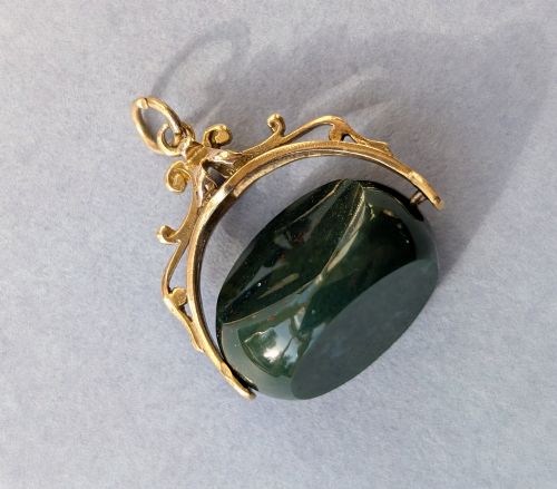 fig 2. An antique 9ct gold spinning fob pendant featuring a polished dark green bloodstone within an ornate scrolled gold swivel frame.