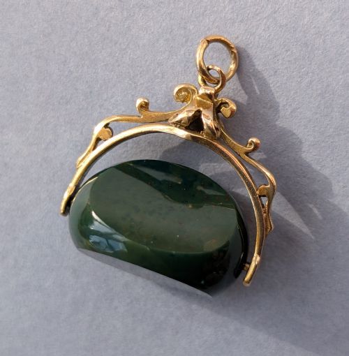 fig 3. An antique 9ct gold spinning fob pendant featuring a polished dark green bloodstone within an ornate scrolled gold swivel frame.