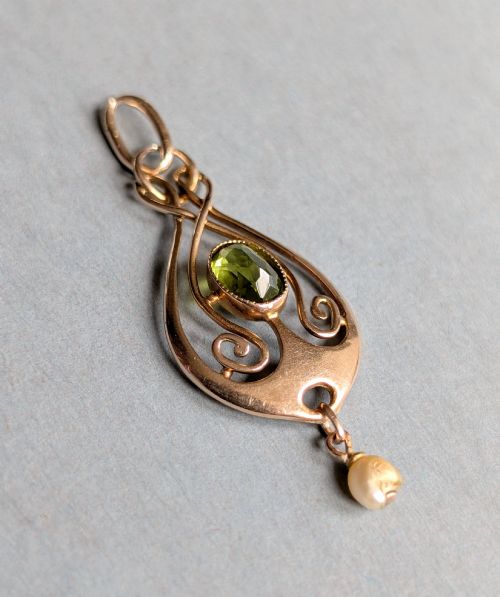 fig 3. An Edwardian 9ct gold openwork Art Nouveau pendant featuring an oval bezel-set green peridot and a suspended pearl drop.