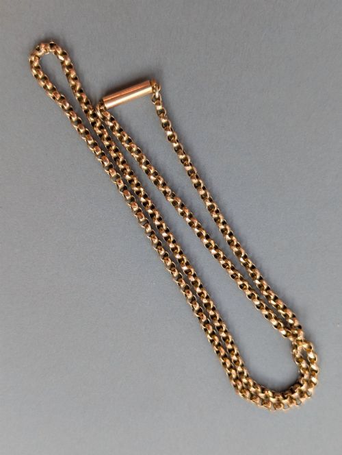 fig 1. An antique 9ct yellow gold belcher chain laid on a plain background showing interlocking rounded links and a barrel fastener.