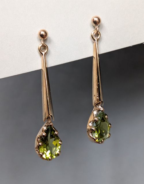 fig 1. A pair of antique 9ct gold drop earrings featuring tapered bars and pear-cut green peridot gemstones suspended from ball posts.