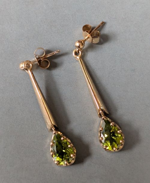 fig 3. A pair of antique 9ct gold drop earrings featuring tapered bars and pear-cut green peridot gemstones suspended from ball posts.