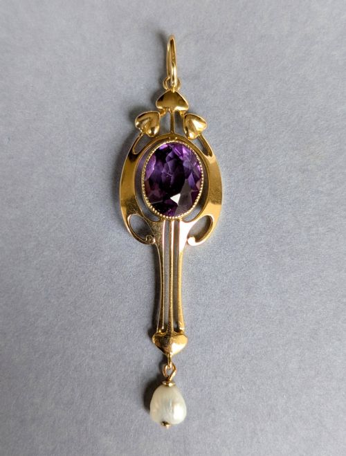 fig 1. An Art Nouveau 15ct gold drop pendant featuring a central oval faceted purple amethyst framed by stylised leaf motifs with a suspended pearl at the base.