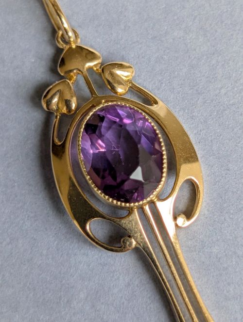 fig 2. An Art Nouveau 15ct gold drop pendant featuring a central oval faceted purple amethyst framed by stylised leaf motifs with a suspended pearl at the base.