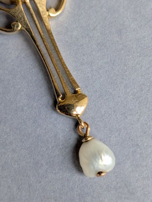 fig 3. An Art Nouveau 15ct gold drop pendant featuring a central oval faceted purple amethyst framed by stylised leaf motifs with a suspended pearl at the base.