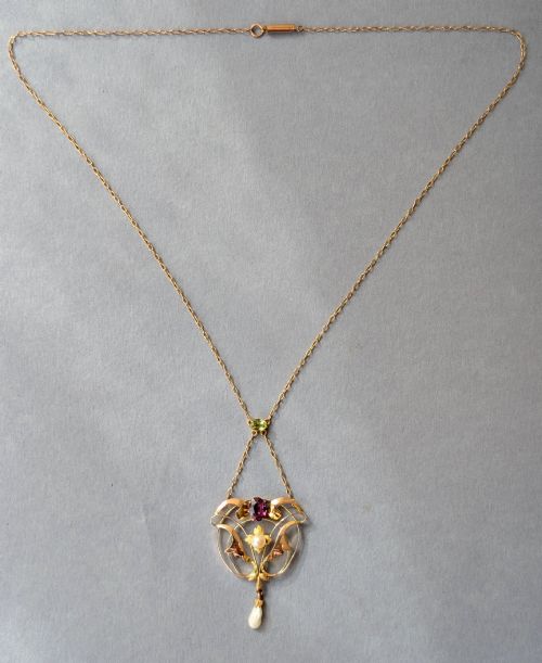 fig 2. An Edwardian openwork gold lavalier pendant set with an oval purple garnet, a seed pearl center, a pearl drop, and a small green peridot, suspended from a gold chain.