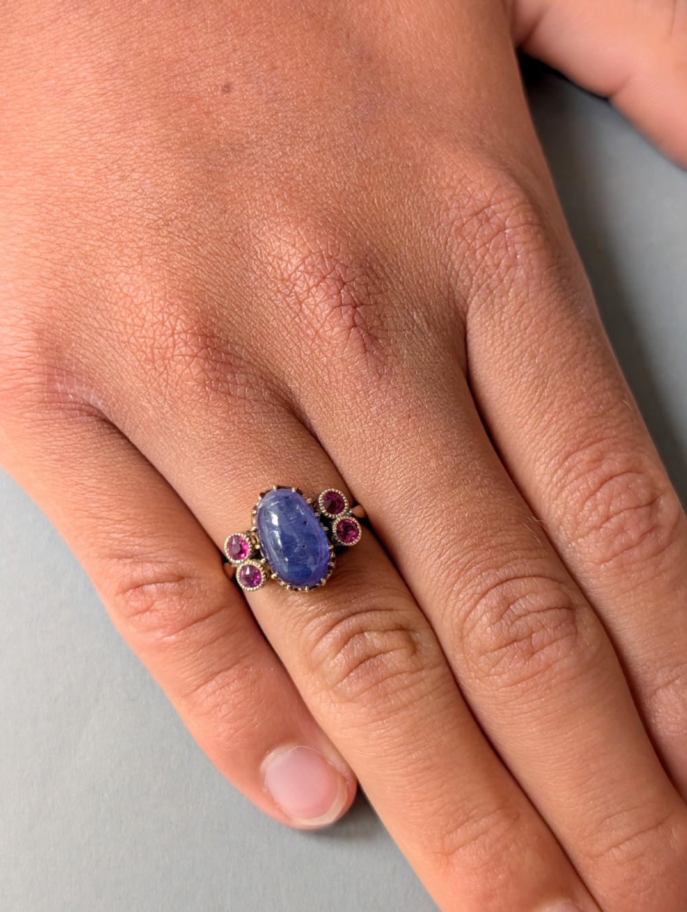 An antique 18ct yellow gold ring featuring a central oval cabochon sapphire flanked by four round faceted rubies in crimped settings. View XIII