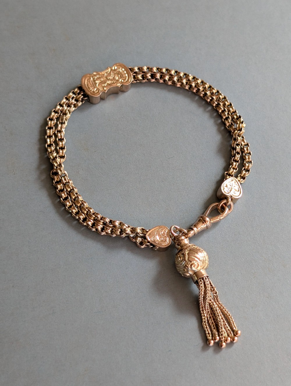 An antique 9ct gold double chain bracelet featuring engraved heart-shaped end pieces, a swivel clasp, and a hanging gold tassel charm. View II