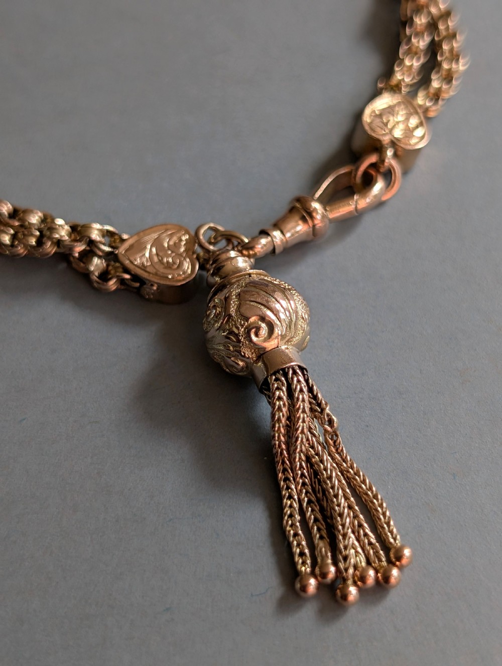 An antique 9ct gold double chain bracelet featuring engraved heart-shaped end pieces, a swivel clasp, and a hanging gold tassel charm. View III